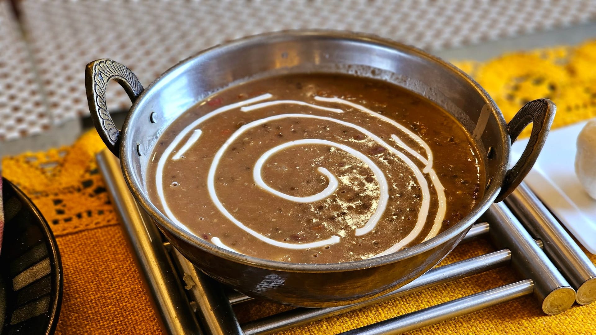 Dal makhani in a steel kadhai on a warming stand, the dark lentils finished with a spiral of cream.