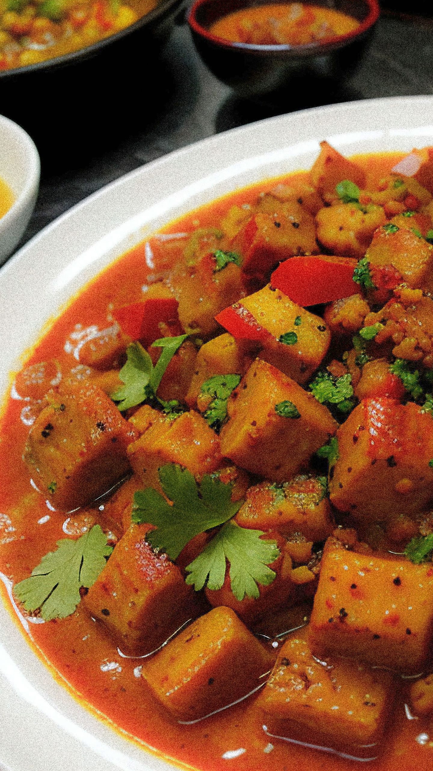 Cubes of paneer in a thick tomato masala with red capsicum and fresh coriander, served in a white bowl.